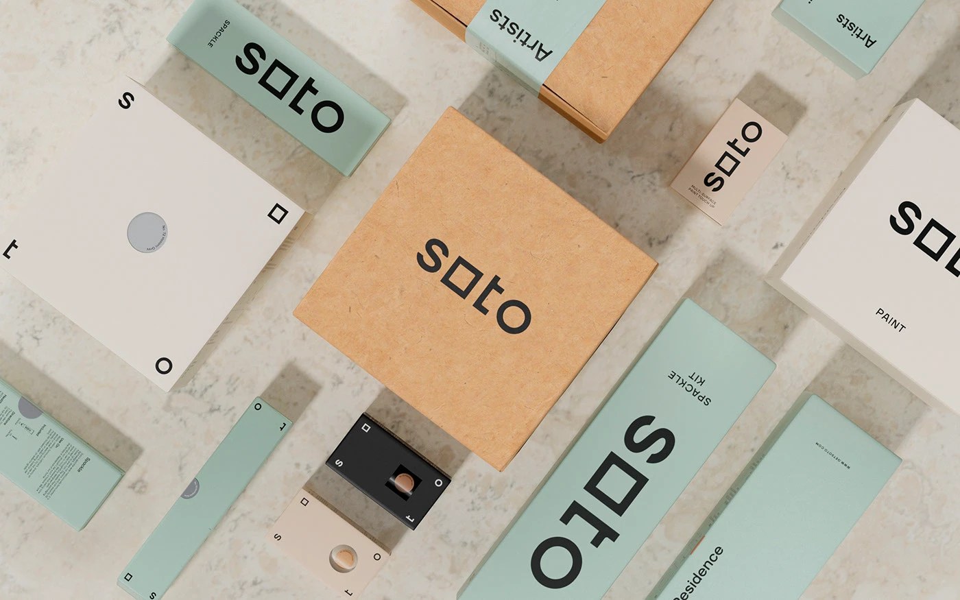 Azulejos de sistema completo marca Soto: caja de papel kraft, kit de enlucido verde salvia, latas de pintura color crema y herramientas sobre mármol blanco